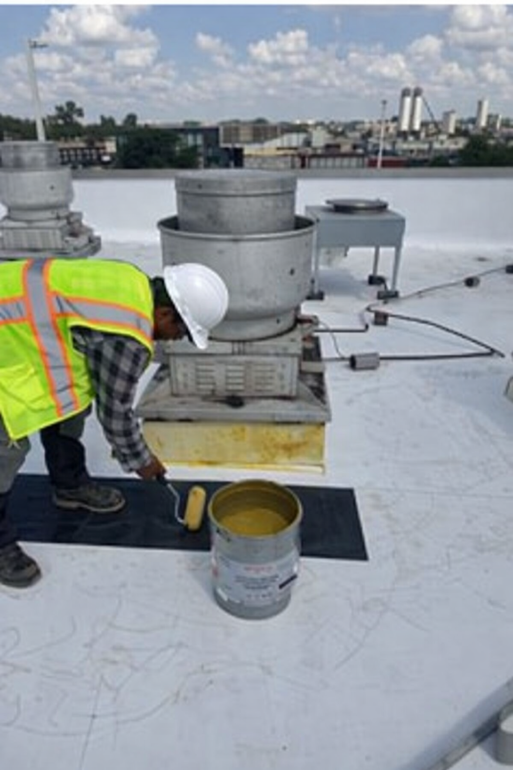 Technician applying flashing sealant around rooftop penetration