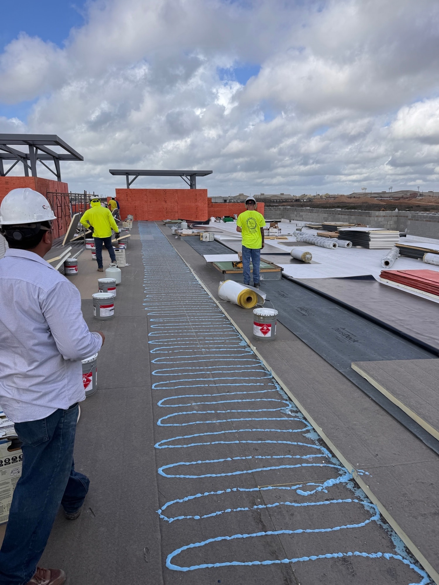 Workers applying adhesive in serpentine pattern for membrane bonding